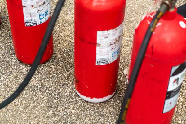 Beton bir yüzeye yerleştirilmiş kırmızı yangın söndürücülerin yakın çekim görüntüsü, acil durum hazırlığı ve yangın güvenliğindeki önemlerini vurguluyor..