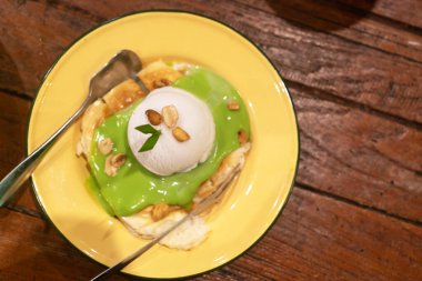 Canlı yeşil bir tepsinin üzerinde bir kepçe dondurmanın bulunduğu nefis bir tatlı, kırsal bir ahşap zemine karşı sarı bir tabakta servis ediliyor. Yemek severler için mükemmel..