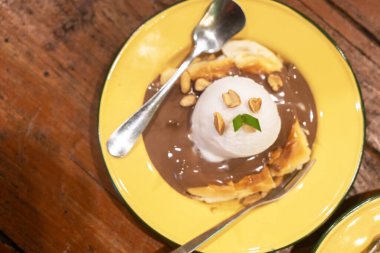 Muz dilimlerinin üzerinde bir kepçe dondurma serpiştirilmiş çikolata soslu ve fıstıkla süslenmiş nefis bir tatlı, tatlı anlar için mükemmel..