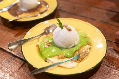 Bu iştah açıcı tatlı, üzerinde canlı yeşil sos ve fındık bulunan bir kepçe dondurmayı her tatlı için mükemmel bir tabakta sunar..