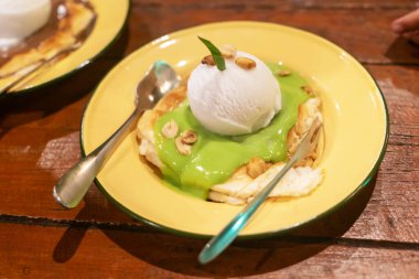 Canlı yeşil soslu krep tabağı, bir kepçe vanilyalı dondurma ve mükemmel bir ikram için çıtır fındık..