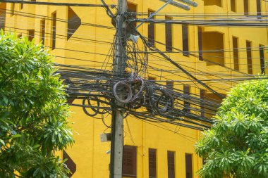 Çevresi yemyeşil ağaçlarla çevrili, kentsel altyapıyı gösteren çarpıcı sarı bir binaya karşı elektrik hatlarıyla dolu canlı bir şehir manzarası..