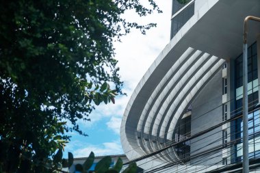 Pürüzsüz kıvrımlı çizgiler ve cam elementlerle donatılmış çarpıcı bir modern mimari tasarım, çevresindeki yeşillik ve mavi gökyüzü ile güzelce zıt düşüyor..