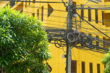 Yeşilliklerle çevrili çarpıcı sarı bir binaya elektrik kablolarının dolandığı canlı bir şehir manzarası. Şehir hayatının mükemmel bir tasviri..