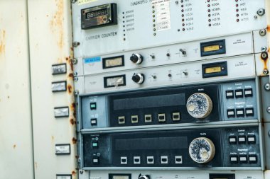 Çeşitli tuşlar, anahtarlar ve ölçüm cihazları içeren karmaşık bir vintage kontrol paneli. Panelde aşınma ve pas belirtileri var, endüstriyel teknoloji sergileniyor..