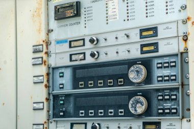 Endüstriyel makinelerin karmaşık tasarımı ve yaşlanmış dokularını vurgulayan çeşitli metre, düğme ve kadranları gösteren vintage kontrol panelinin yakın görüntüsü.