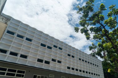 Çarpıcı bir modern mimari tasarım, yakınlardaki ağaçların verimli yeşillikleriyle tamamlanmış bulutlara karşı benzersiz bir cephe sergiliyor..