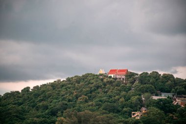 Dramatik bulutlu bir gökyüzünün altında yemyeşil ve canlı mimarisi olan sakin bir manzarayı gözler önüne seren bereketli bir tepeye tünemiş dingin bir tapınak..