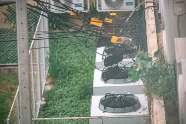 Görünür elektrik kabloları ve kabloları olan konut ortamındaki havalandırma ünitelerinin görüntüsü. Yeşil çimen ve kentsel ayrıntılar arkaplanı güçlendirir.