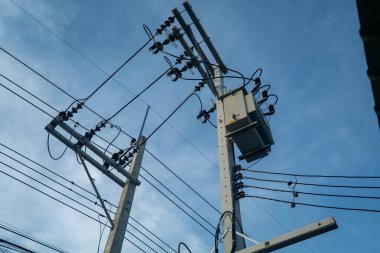 Açık mavi gökyüzüne elektrik direğine bağlı elektrik hatlarının güzel görüntüsü, kentsel ve kırsal bölgelerdeki temel elektrik dağılımını sembolize ediyor.