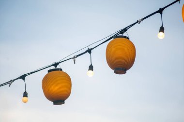 Işıldayan turuncu fenerlerin çekici bir sahnesi yumuşak bir akşam gökyüzüne karşı bir çizgi boyunca dizilmiş. Kutlama ve açık hava dekorasyonu için mükemmel..