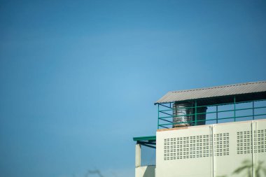 Eşsiz bir çatı tasarımına sahip modern bir endüstriyel bina açık mavi gökyüzüne karşı duruyor, mimari detaylarını ve endüstriyel cazibesini vurguluyor..