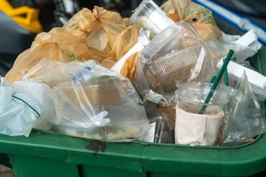 Plastik atık, yemek artıkları ve poşetlerle dolu bir çöp kutusunun yakın çekim görüntüsü. Bu resim kentsel alanlardaki çevre kirliliği ve atık yönetimi sorunlarını vurgular.