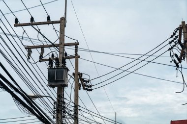 Gri gökyüzüne karşı elektrik hatları ve elektrik direklerinden oluşan bir ağ, kentsel bir ortamda karmaşık elektrik dağıtım ve altyapı sistemini sergiliyor..