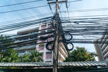 Şehir altyapısının, elektrik bağlantılarının ve telekomünikasyonun karmaşıklığını gözler önüne seren, şehir manzarasının üzerindeki karmaşık kabloların çarpıcı görüntüsü.