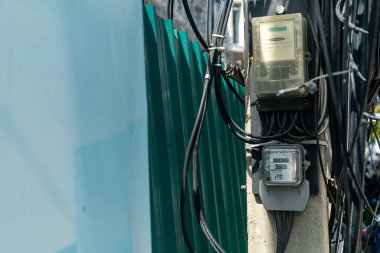 Elektrik direğine bağlı elektrik sayacının ayrıntılı görüntüsü, elektrik kabloları, kablolar ve şehir ayarları. Enerji ve altyapı temaları için ideal.