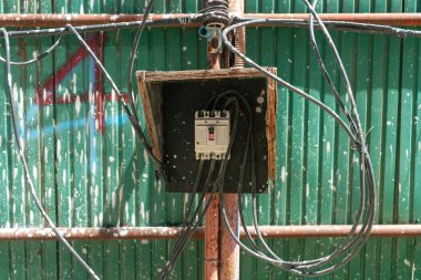 Kumaşlı yeşil arka plan, kentsel bozulma ve endüstriyel tasarım elementlerini gösteren açık kablolu bir elektrik kontrol kutusu..