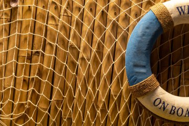 Canlı bir yaşam halkası, kıyı tasarımı meraklıları için deniz temalı mükemmel bir dekor oluşturan, bir balıkçı ağıyla çevrili, kırsal ahşap bir duvara dayanır..