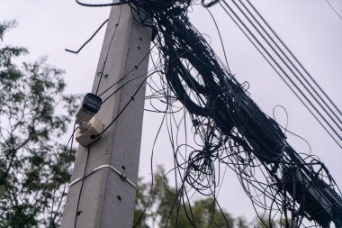 Karmaşık kablolar ve kablolar yüklü bir elektrik direğinin yakın çekim görüntüsü. Şehir merkezinde bir güvenlik kamerası var..
