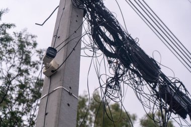 Bu görüntü, kentsel altyapı ve izleme teknolojisinin karmaşıklığını vurgulayan kaotik kablo ve kablo düzenine sahip bir elektrik direğini gösteriyor..