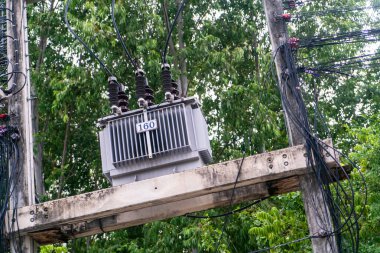 Tahta bir elektrik direğine monte edilmiş, birden fazla elektrik kablosuyla çevrili transformatörün detaylı bir görüntüsü. Bu resim temel elektrik altyapısını gösteriyor.