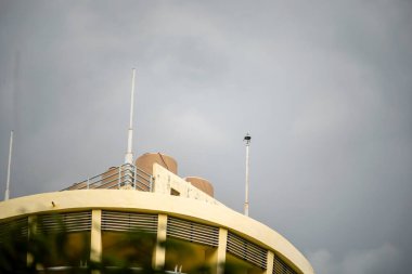Modern bir binanın çatısının bulutlu bir gökyüzüne karşı çarpıcı bir görüntüsü, mimari detaylar ve çağdaş yaşamın özünü yansıtan kentsel tasarım unsurları içeriyor..
