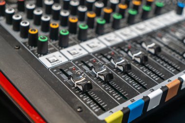 Stüdyolarda ve canlı ortamlarda ses miksajı ve müzik üretimi için gerekli olan çeşitli düğmeleri ve kaydırakları gösteren profesyonel bir ses karıştırma konsolunun yakın görüntüsü.
