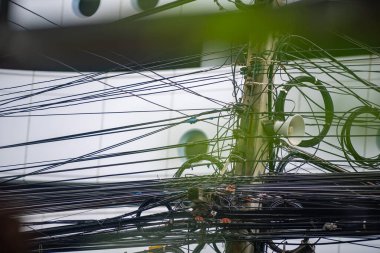 Şehir ortamında elektrik kablolarının ve elektrik kablolarının birbirine dolanmış görüntüsü modern elektrik ağlarının karmaşıklığını gösteriyor..