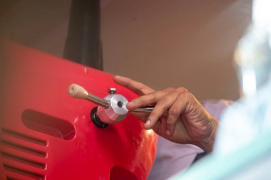 Kırmızı bir makinenin kontrol kolunu kullanan bir eli gösteren yakın plan bir görüntü. Endüstriyel çalışmalardaki hassasiyet ve manüel beceriyi vurguluyor.