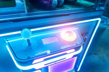 Bu resim, eğlence ve etkileşimli oyun deneyimlerini vurgulamak için mükemmel, bir joystick ve parlayan düğme içeren parlak ışıklı bir oyun kontrol paneli yakalar..