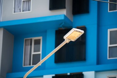 Modern bir sokak lambası parlak mavi bir binaya karşı duruyor, şehir mimarisini ve şehir yaşamındaki ışık ve tasarımın etkileşimini sergiliyor..