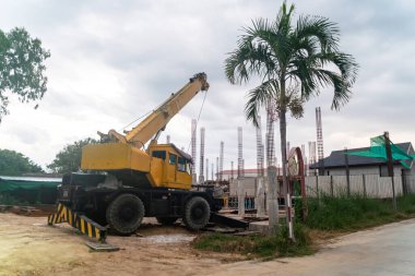 Bir inşaat vinci, palmiye ağaçları ve yükselen yapılarla çevrili bir kentsel alanda duruyor. Geliştirme çalışmaları sırasında makineleri çalışırken gösteriyor..