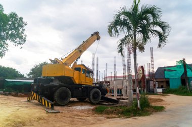 Mobil bir inşaat vinci, inşaat projelerinde ve kentsel gelişimde kullanılan makineleri gösteren bir palmiye ağacının yakınındaki bir şantiyeye park edilmiştir..