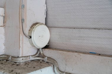 Duvarın yanında eski beyaz bir elektrik bağlantısı görülür. Çamur ve giysi sergilenir. Bu resim, yerli elektrik tesisatı ve bakım konularının ayrıntılarını vurgular.