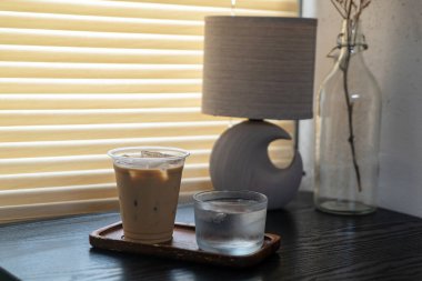 Rahatlatıcı bir buzlu kahve ve ahşap bir masanın üzerinde bir bardak su bulunan sıcak bir ev atmosferini geliştiren, rahatlatıcı anlar için mükemmel bir sahne..