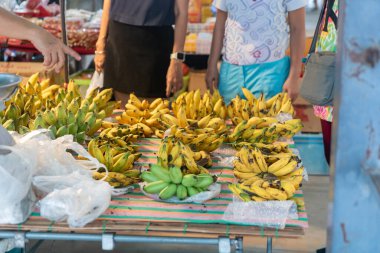 Yerel bir markette renkli, taze muz gösterisi. Alışverişçilerin canlı bir yiyecek kültürünün atmosferine girmesiyle çeşitli olgunluklar sergiliyor..