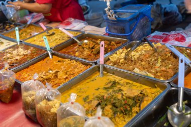 Kalabalık bir markette çeşitli tabaklar sunan renkli sokak yemekleri. Canlı sunum yemek severleri eşsiz tatları keşfetmeye davet ediyor..