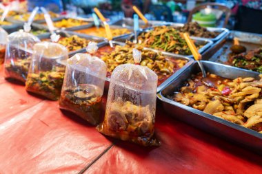 Naylon poşetlerde sunulan taze sokak yiyeceklerinin canlı bir sahnesini keşfedin, kalabalık bir açık hava pazarından çeşitli yemekler sergilenmektedir..