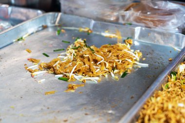 Metal bir tepside taze pişmiş eriştenin yakın plan görüntüsü, canlı malzemeler ve sokak yemeği kültürünün tipik yemek pişirme tarzını gösteriyor..