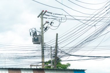 Bulutlu bir gökyüzüne karşı sayısız elektrik hattı ve kablosu olan elektrik direğinin görüntüsü, kentsel altyapı ve elektrik dağıtımı.