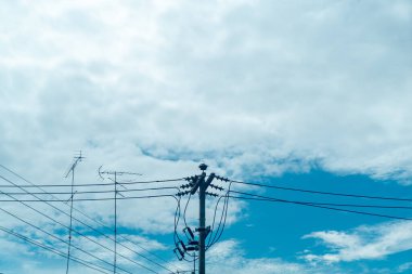 Kabarık bulutlarla lekelenmiş mavi gökyüzü üzerindeki elektrik hatlarının net bir görüntüsü. Bu resim modern altyapıyı ve doğal güzelliği uyum içinde sergiliyor..