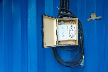 Canlı mavi bir yüzeye monte edilmiş elektrik bağlantı kutusu, kablolar ve aletler sergiliyor. Elektrik işi, güvenlik ve hizmet tesisleri hakkındaki kavramlar için ideal.