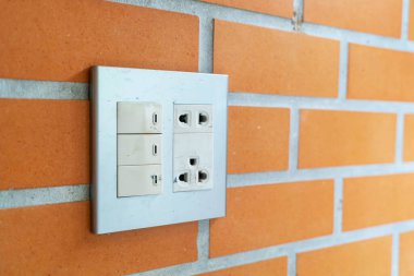Dokulu tuğla bir duvara monte edilmiş bir elektrik prizinin yakın plan görüntüsü, iç düzende kullanım ve modern iç tasarım unsurlarının bir karışımını gösteriyor.