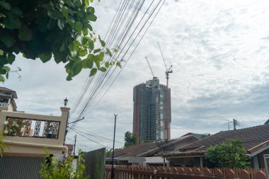 A captivating cityscape featuring a modern building under construction, highlighting cranes, nearby homes, and an expansive sky, showcasing urban development.