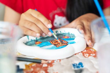 A child engages in painting a colorful plate with watercolors, showcasing creativity and artistic skill. Close-up of hands in a leisure activity.