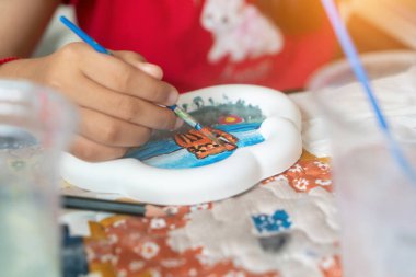A young child enjoys painting a ceramic plate outdoors, capturing a vibrant scene and showcasing creative skills. A joyful and engaging activity.
