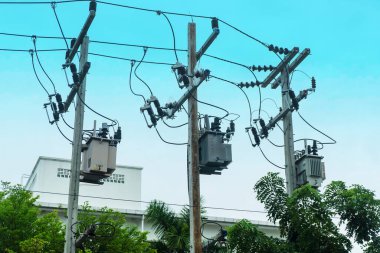 Detailed view of power distribution infrastructure in an urban area, showcasing utility poles, overhead cables, transformers, and surrounding landscape elements.