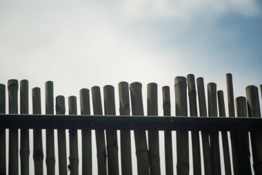 A striking silhouette of a bamboo fence stands against a cloudy sky, showcasing natural beauty and simplicity in outdoor architecture and design.