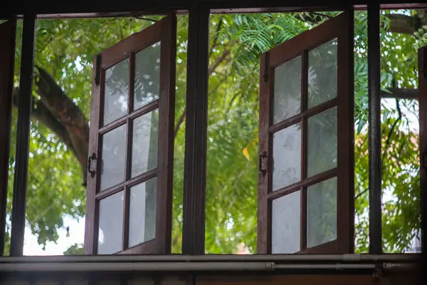 Captivating rustic wooden windows open to a lush greenery view, inviting natural light and a sense of tranquility into the interior space.