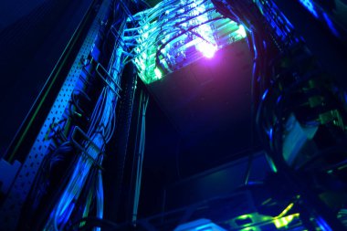 Canlı mavi ışıklarla aydınlatılmış bir sunucu dolabının detaylı bir görüntüsü. Bu resim, modern teknoloji ve altyapıyı vurgulayan kablolar ve bağlantılar sergiliyor.